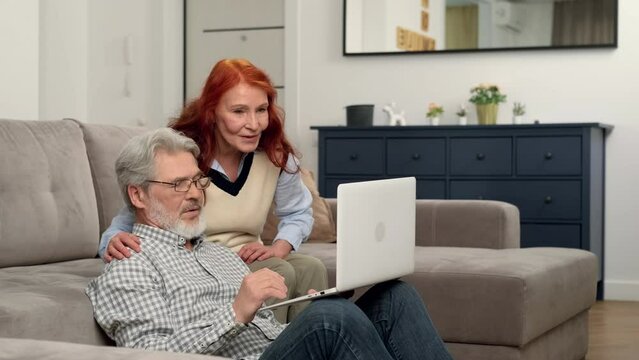 Happy senior couple aged 60-70 make an online purchase at home using a laptop.