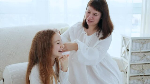 Young mother and cute red hair 6 years old daughter are having fun at home in the morning. Mom kisses happy daughter while she laughing, 4k video