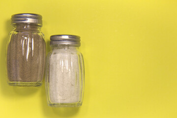 Salt and pepper in salt shakers. On a yellow background. Place for text.