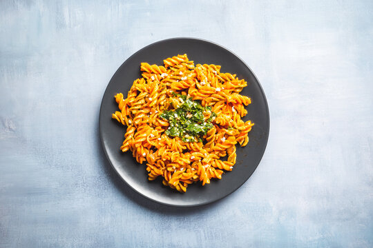 Curly pasta macaroni with tomato and gremolata sauce in a round dark plate on a table. Ready to eat.