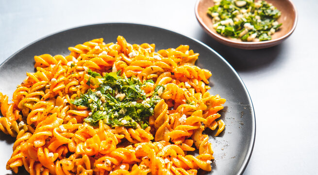 Curly pasta macaroni with tomato and gremolata sauce in a round dark plate on a table. Ready to eat.