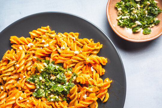 Curly pasta macaroni with tomato and gremolata sauce in a round dark plate on a table. Ready to eat.