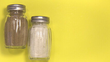 Salt and pepper in salt shakers. On a yellow background. Place for text.