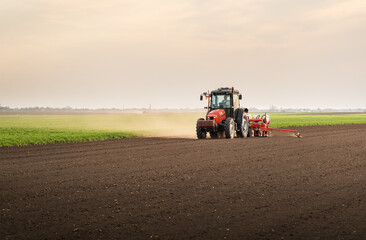 Farmer with tractor seeding - sowing crops at agricultural field