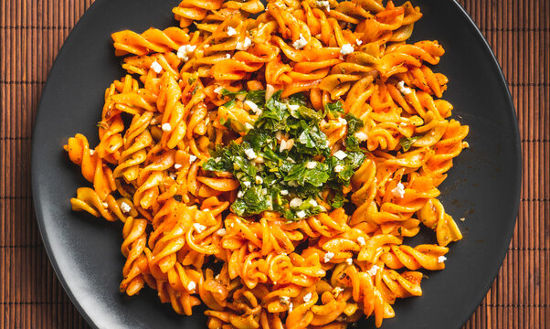 Curly pasta macaroni with tomato and gremolata sauce in a round dark plate on a table. Ready to eat.
