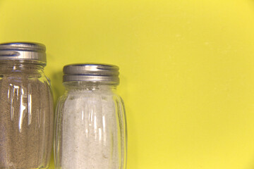 Salt and pepper in salt shakers. On a yellow background. Place for text.