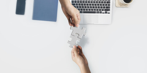 Two hand joining two matching puzzle pieces on desk background, conceptual image of teamwork.