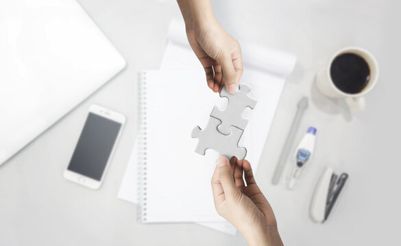 Two hand joining two matching puzzle pieces on desk background, conceptual image of teamwork.