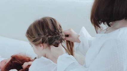 Young woman braids her little daughter while she plays with a doll, rear view close-up 4k footage. Maternity and mother's day concept.