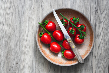 Rote Cocktailtomaten in einer rustikalen Schüssel und ein Messer auf einem braunen Holztisch. Draufsicht, Gemüse.