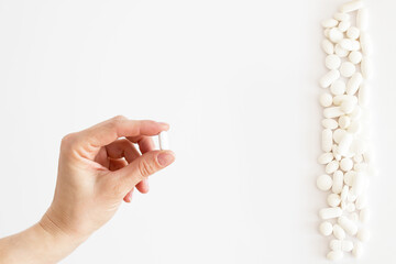 Biała tabletka trzymana w dłoni, białe lekarstwa i witaminy w tabletkach rozsypane na jasnym tle, suplementacja diety, leczenie przewlekłe, farmacja - 500394829