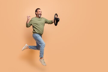 Full length profile photo of excited cheerful man look empty space vehicle wheel isolated on beige color background