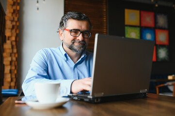 Business, technology and people concept , senior businessman with laptop computer drinking coffee at modern cafe.