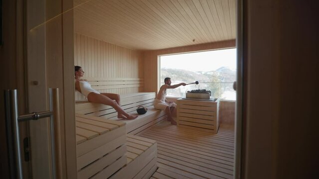 Handsome young couple relaxing in the sauna and watching winter forest through the window