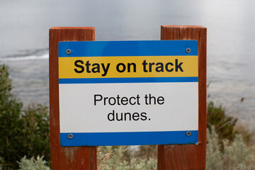 Fototapeta premium Sign near the beach advising to stay on the track and protect the sand dunes above Howrah Beach