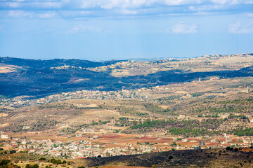 Fototapeta na wymiar Spring Israeli landscape. View from the mountain to a hilly valley with villages, fields and gardens. Clouds cast shadows on the ground.