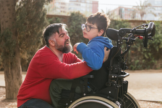 Loving father playing and enjoying time with his son with disability in a wheelchair.