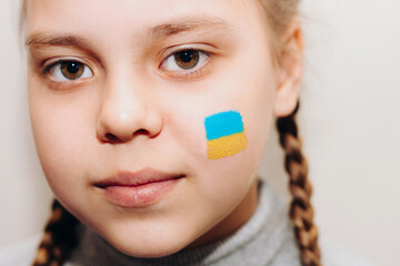 Close-up portrait of a girl, a blue-yellow drawing of the flag of Ukraine is drawn on her cheek.