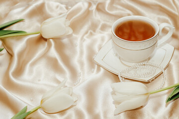 Bouquet of white tulips with pearl beads and tea on silk golden nude satin background.