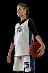 Portrait of teen girl, basketball player in uniform posing isolated over black studio background. Team leader