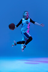 Fototapeta na wymiar Throwing ball into basket. Portrait of teen girl, basketball player training, scoring a goal isolated over blue background in neon.