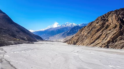 Papier Peint photo Dhaulagiri A view on a dry bottom of Himalayan valley. The valley is located in Mustang region, Annapurna Circuit Trek in Nepal. In the back there is snow capped Dhaulagiri I. Barren and steep slopes