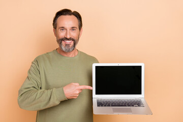 Portrait of attractive trendy cheerful man demonstrating laptop copy space ad isolated over beige...