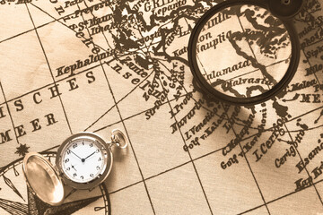 Pocket watch on old map background, vintage style light and tone.Travel, geography, navigation, tourism and exploration concept background. Macro shot, shallow focus.