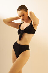 Obraz premium Fashion photo of young lady with perfect body in a black designer trend 2022 swimsuit. Girl on a sunny day sunbathes in sexy pose on the white. Sun screen, summer concept.