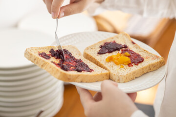 hand apply sweet berry fruit jam on a sliced whole wheat bread for breakfast high energy meal in...
