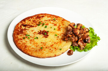 traditional Swiss dish is a potato pancake on a white plate with fried mushrooms and a leaf of green lettuce, close-up.