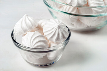 dessert of French meringue lies in a glass bowl on a light background. in the background there is another candy bowl with meringue. Meringue is made from a mixture of whipped egg whites with sugar.