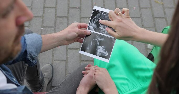 Close-up top view of a woman showing an ultrasound image to her husband. A couple in love is expecting a baby