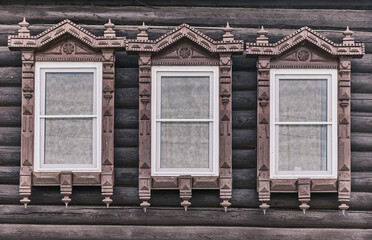 Wndows with carved wooden architraves. Log facade of typical rural Russian house.