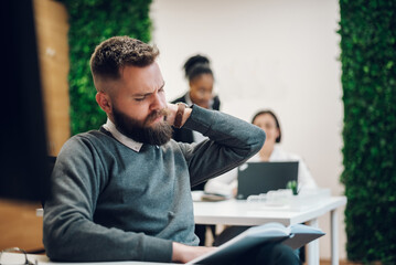 Businessman suffering from neck pain while sitting at the office desk