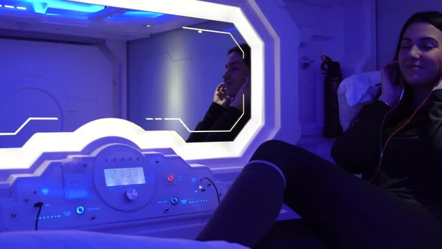 Spanish female traveler lying on the capsule hotel bed, listening to music with her headphones and dancing.