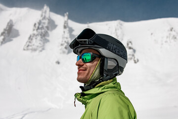 man in sunglasses and a ski helmet against the backdrop of snow-capped mountains
