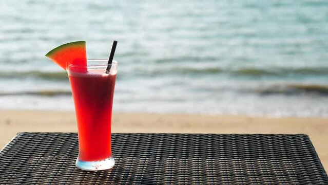 Fresh watermelon juice on tropical summer beach. Vacation, travel or holiday concept. Fruit cocktail on background of sea waves. Sea view with tall drinking glass with healthy shake on table.
