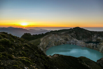 Sunrise over the Kelimutu volcanic crater lakes in Moni, Flores, Indonesia. Skyline is bursting with orange. Turquoise color of the lake. Golden hour colours the surroundings. Beauty of the nature - obrazy, fototapety, plakaty