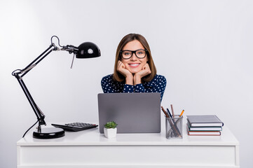 Photo of cheerful positive person hands on chin sit behind workstation isolated on grey color...