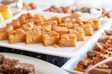 Semolina cake, or Revenue, Revani or Ravani. Made from a combination of semolina and flour and soaked in a citrus infused syrup. Various cakes and sweets on buffet