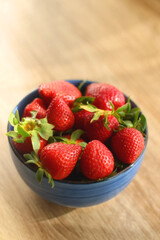 Bowl of fresh strawberries on wooden table, illuminated by sunlight. Selective focus.