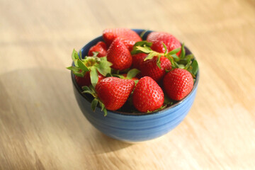 Bowl of fresh strawberries on wooden table, illuminated by sunlight. Selective focus.