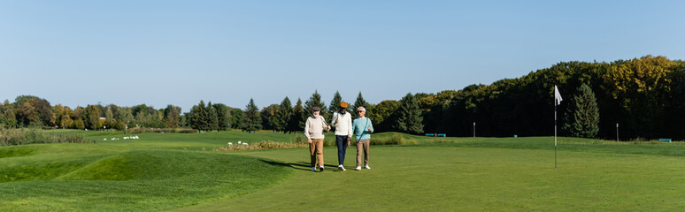 asian man in sunglasses walking near senior multiethnic friends with golf clubs, banner.