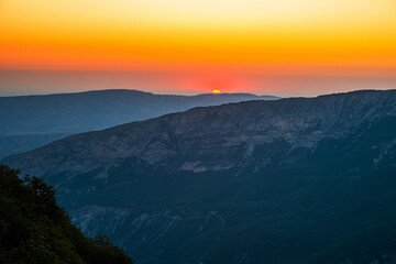 Amazing sunset over mountain range, scenic alpine landscape with dark silhouettes of mountains, fiery yellow sky and sun