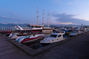 Boats, yachts in the harbor against the backdrop of snow-capped mountains at dusk, Batumi