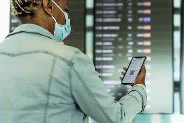 African senior woman checking her flight on mobile smartphone wearing face mask during coronavirus pandemic