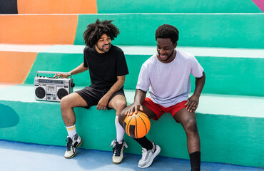 Happy African American friends listening music inside basketball court with vintage boombox stereo...