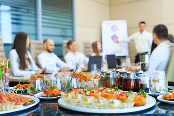 Catering in the office. A table with canapes and various snacks served  on the background of a business meeting.