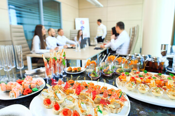 Catering in the office. A table with canapes and various snacks served  on the background of a business meeting.